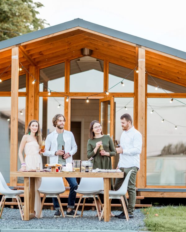 Four friends enjoying evening time together drinking beer on the backyard of the modern country house