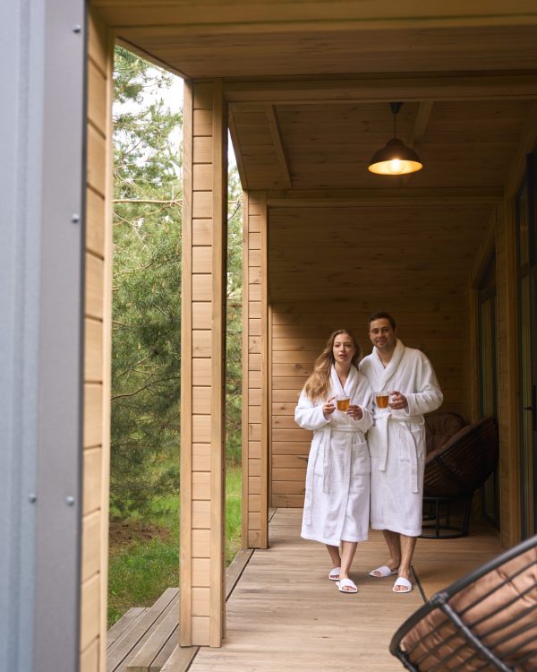 Handsome man and beautiful woman in white bathrobes embracing and drinking fresh relaxing tea